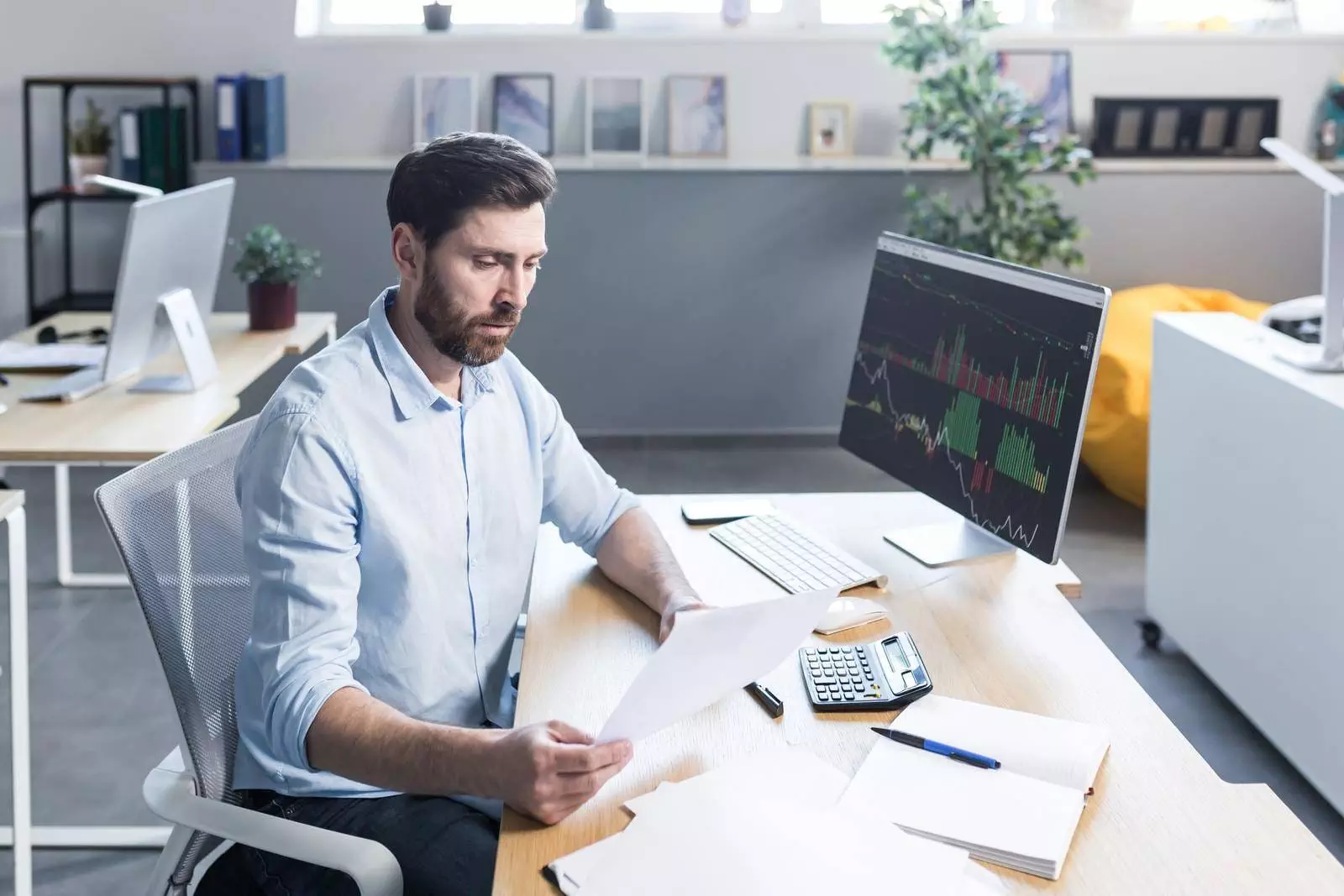 Confident business man stocks broker sitting in front of monitor screen in office analyzing