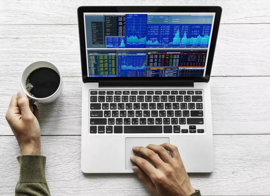 Hands visible on the image frame tracking stock trading through a laptop while having a coffee.