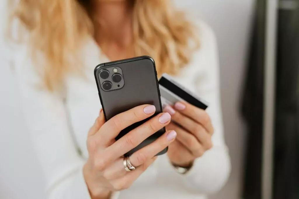 Woman transferring money from a bank card to iPhone, indicating a dematerialized account transaction.